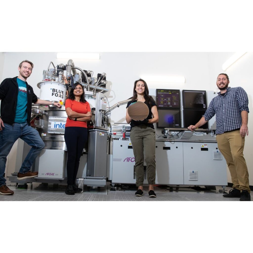 Intel's Quantum Engineers Florian Luthi (from left), Aditi Nethwewala, Stephanie Bojarski and Otto Zietz stand in front of a van sized tool called a cryoprober, which sits in a lab at Gordon Moore Park at Ronler Acres in Oregon. In the cryoprober's chamber, 300-millimeter silicon wafers are tested at 1.7 kelvins, just above absolute zero. Bojarski holds one of those 300-millimeter spin qubit wafers. (Image from Intel Corporation)